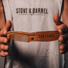 Wooden folding beard comb with Stove & Barrel engraving, held by man in branded apron
